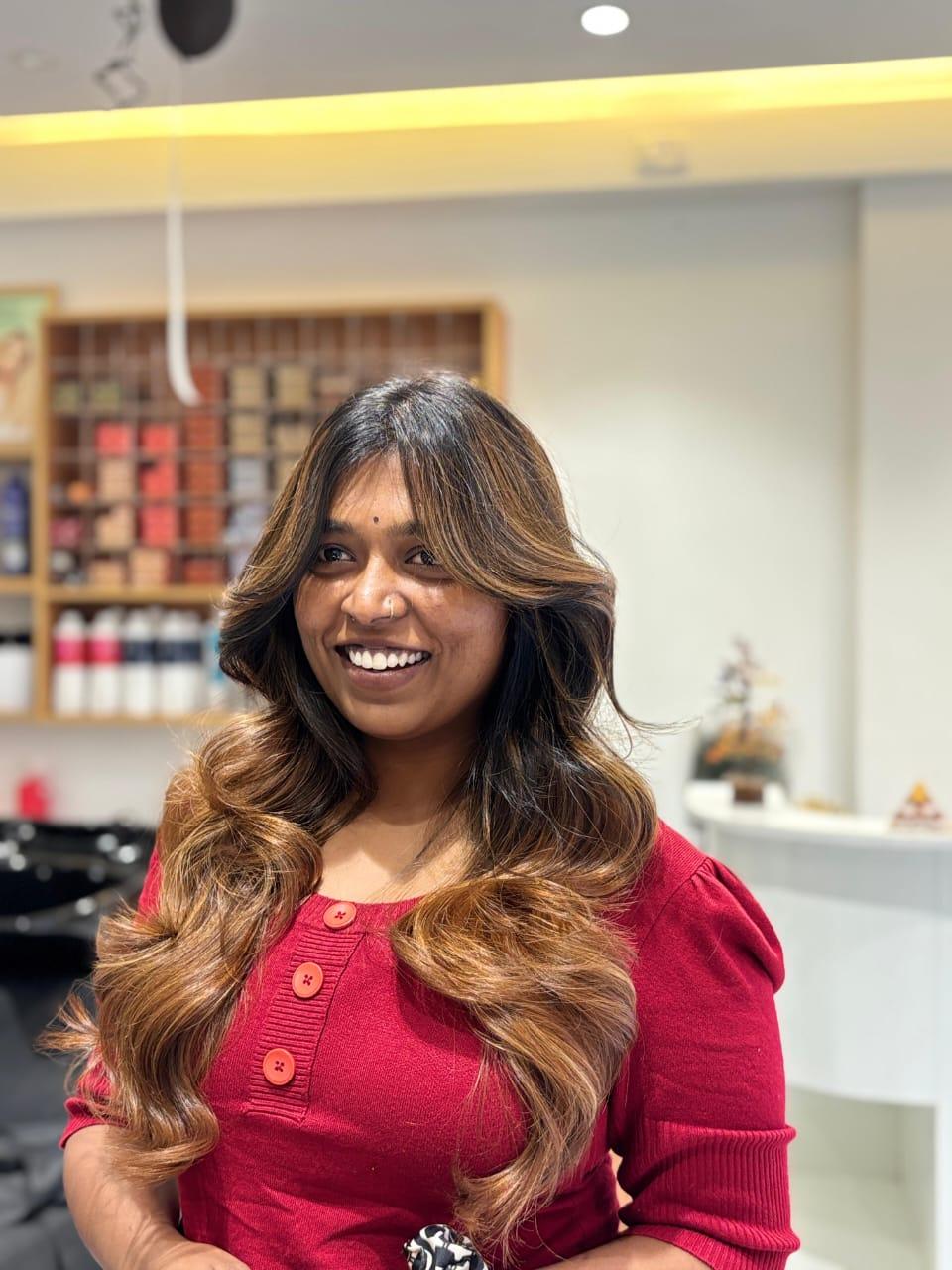 Happy client with voluminous caramel balayage waves and curtain bangs at TRÈS BON Salon